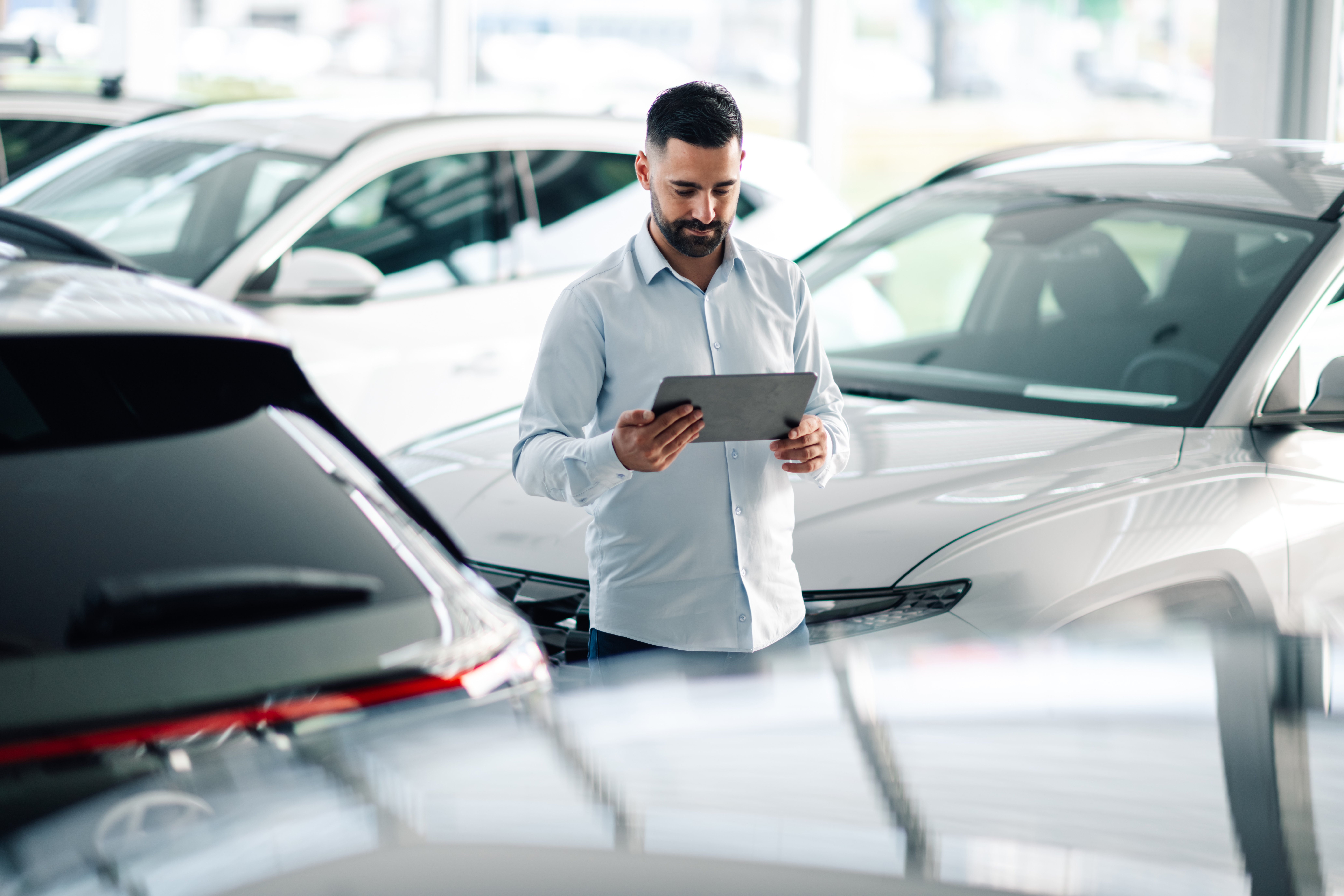 Car salesman using digital tablet while working in auto showroom